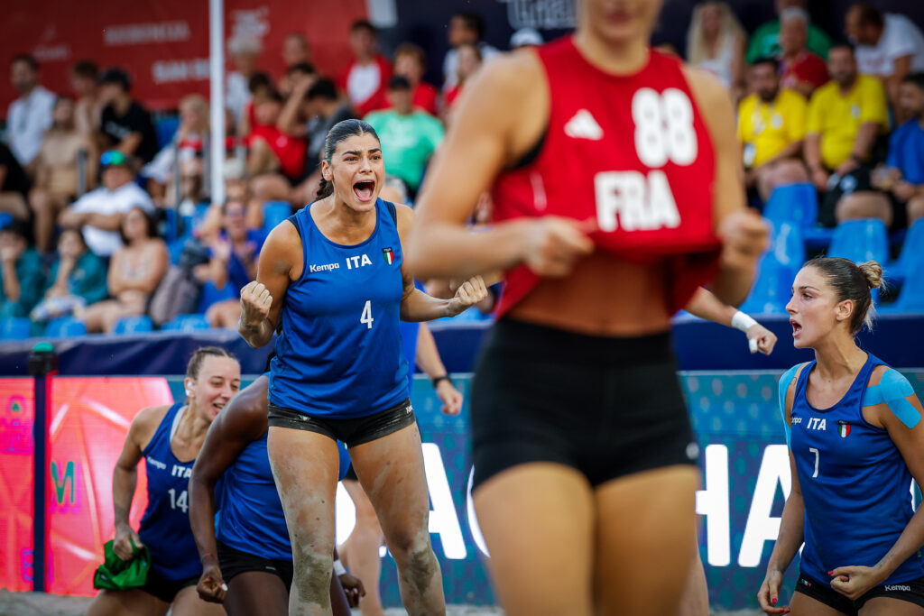 A volleyball player in a blue jersey with the number 4 celebrates enthusiastically on the court while teammates and opponents are visible nearby.