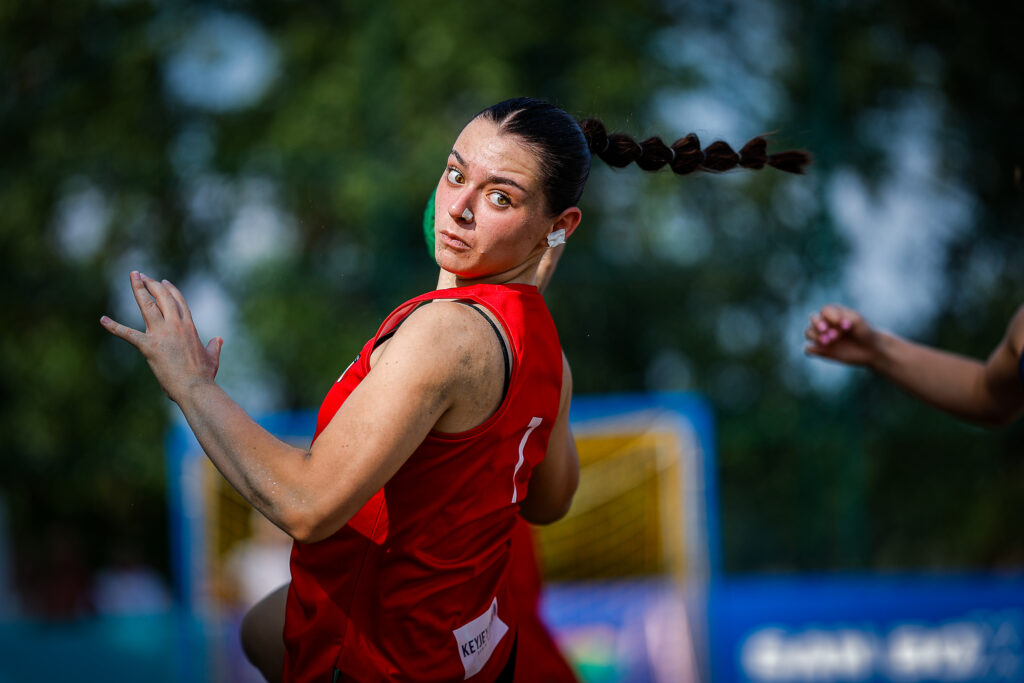 An athlete in a red jersey prepares to throw a discus during an outdoor competition, with a braided ponytail and focused expression.